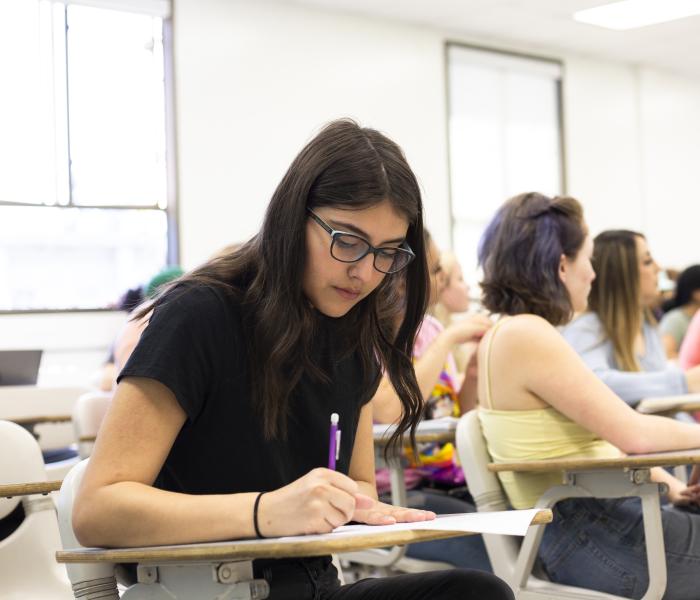 A female student seated in a classroom takes notes.