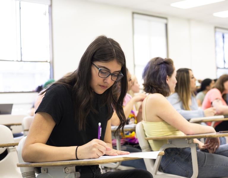 A female student seated in a classroom takes notes.